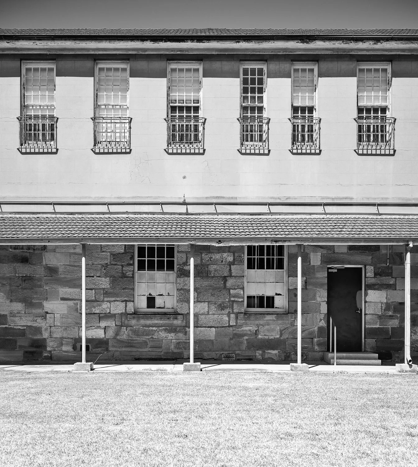 Black and white photo of a two-story building with barred windows, stone and stucco walls, and a grassy front yard.