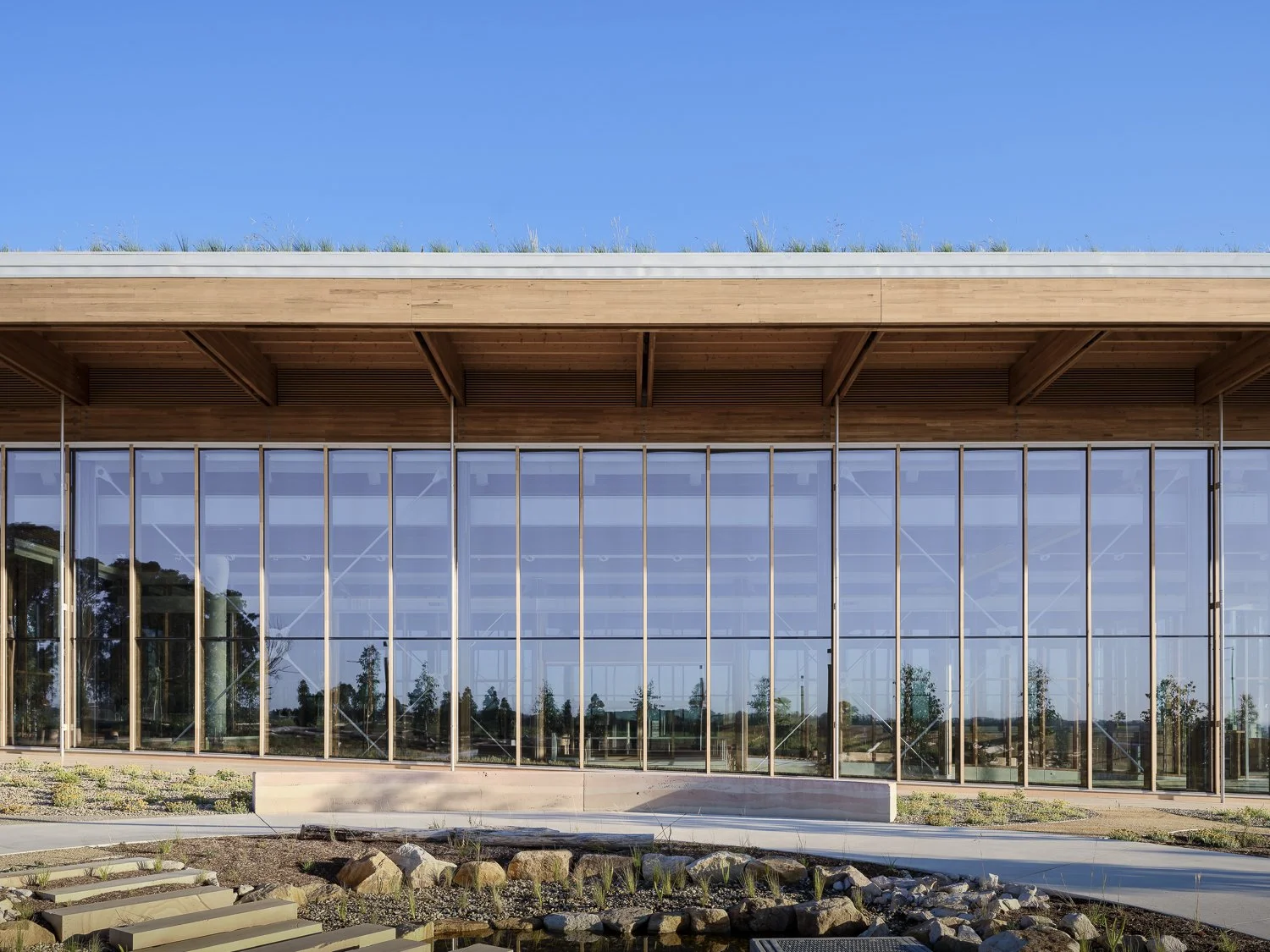 Modern glass building with wooden accents and a landscaped foreground under a clear blue sky.