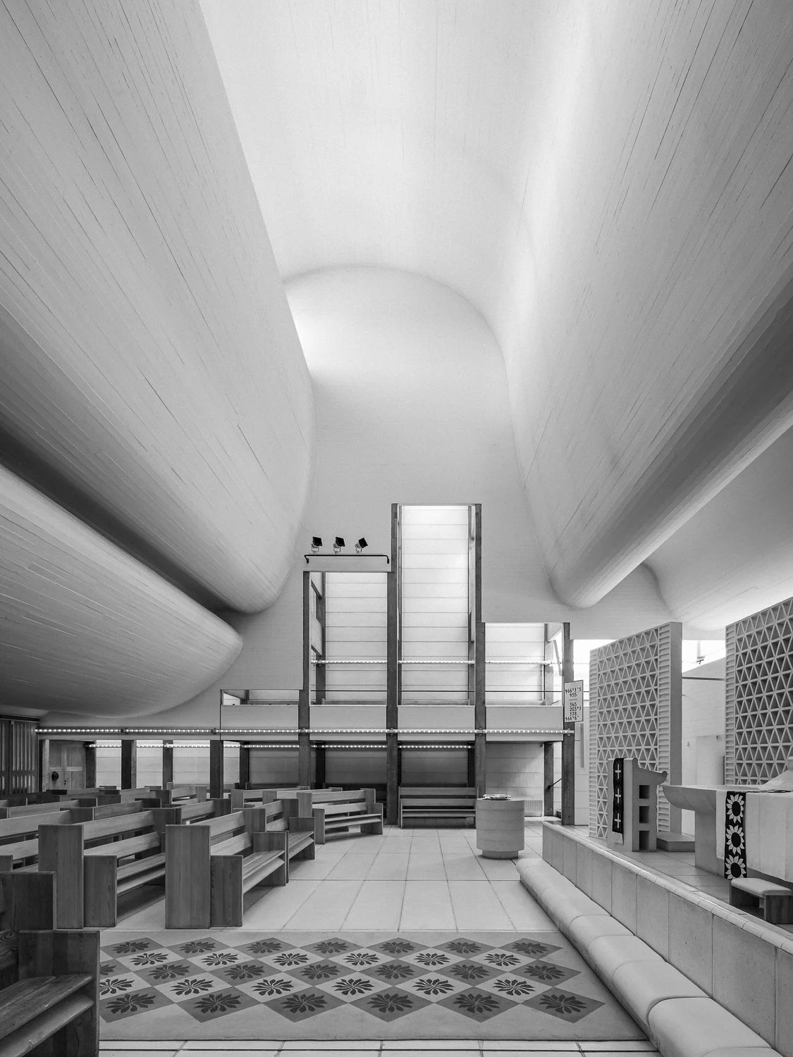 Interior of a modern church or chapel with curved ceiling, wooden benches, and a central altar area.