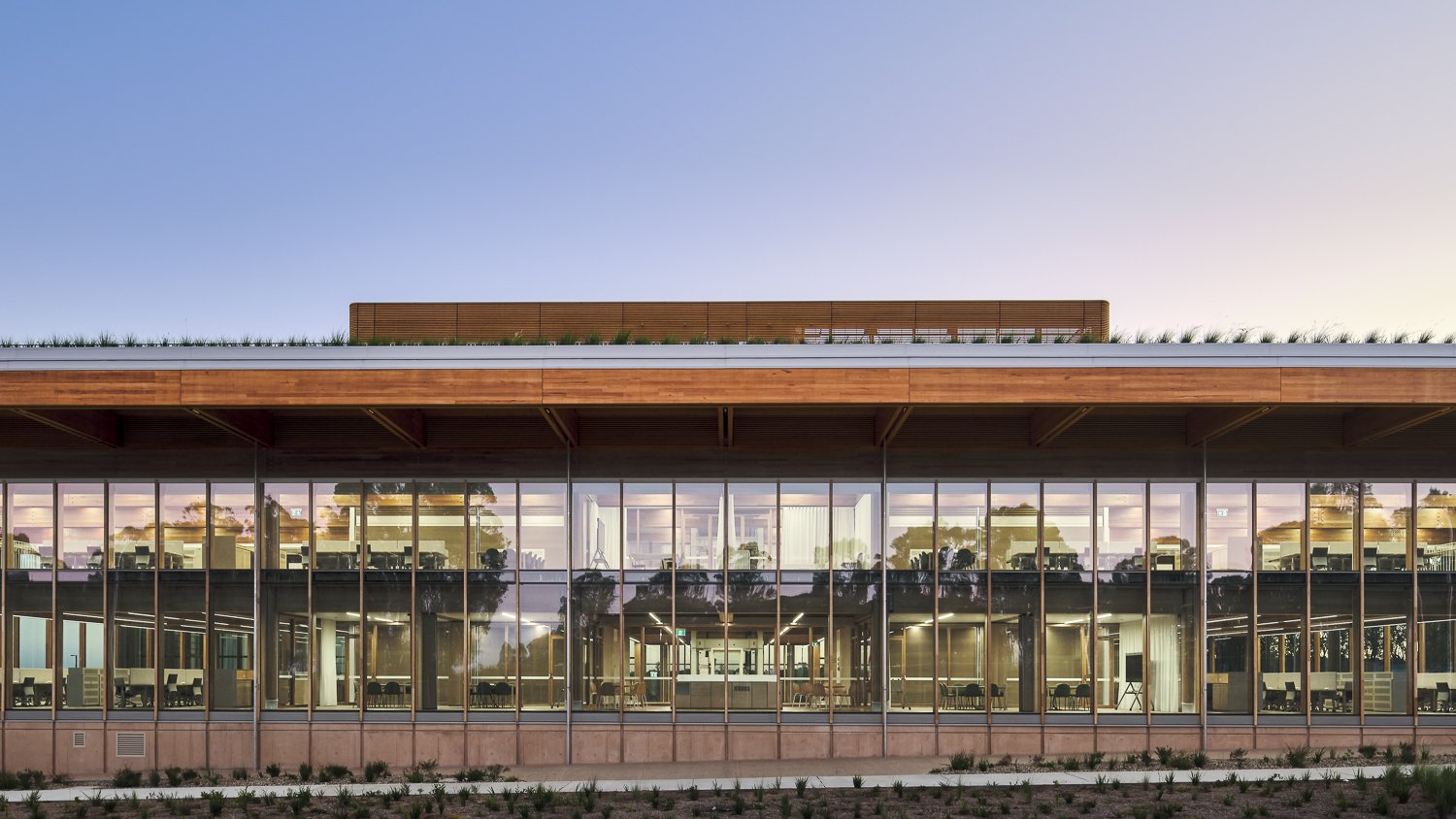 Modern building with large glass windows, wooden accents, and rooftop plants.