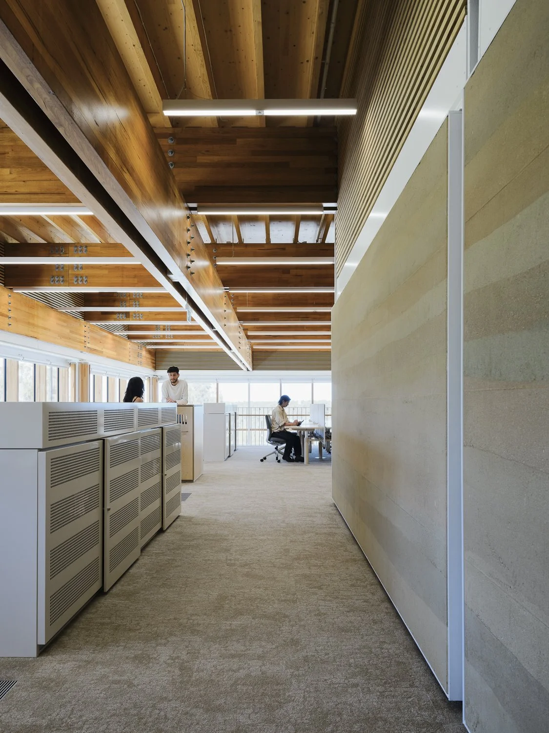 Modern office space with wooden ceiling, glass windows, and people working at desks.