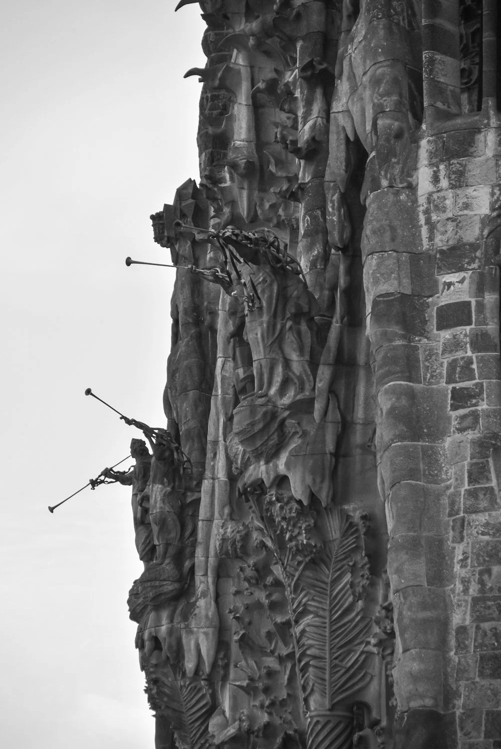 Black and white photo of a monument with three large statues of soldiers holding rifles, mounted on a stone wall with decorative leaf carvings.