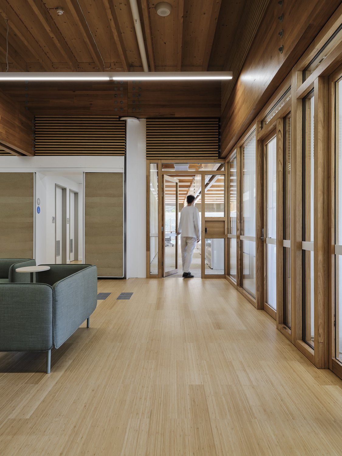 Modern office lobby with wooden accents, large glass windows, and a person walking through a glass doorway.