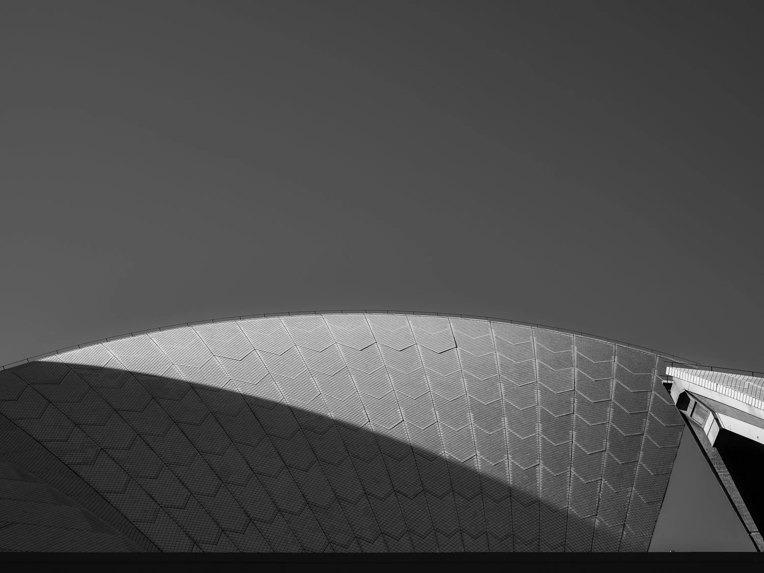 A modern, curved building with a geometric pattern on its exterior, seen against a cloudy sky.