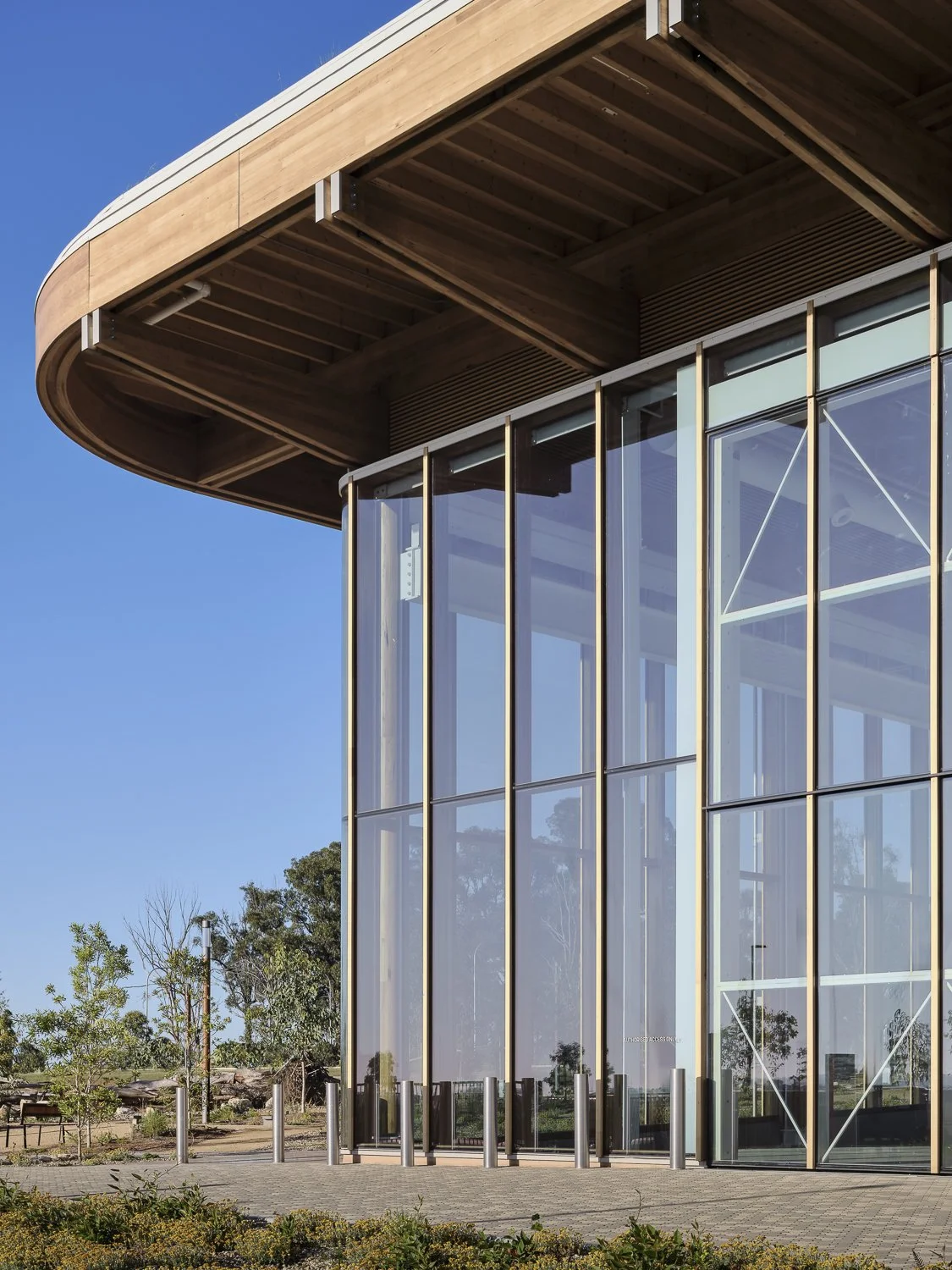 A modern building with a curved roof, large glass windows, and metal framing, set against a clear blue sky.