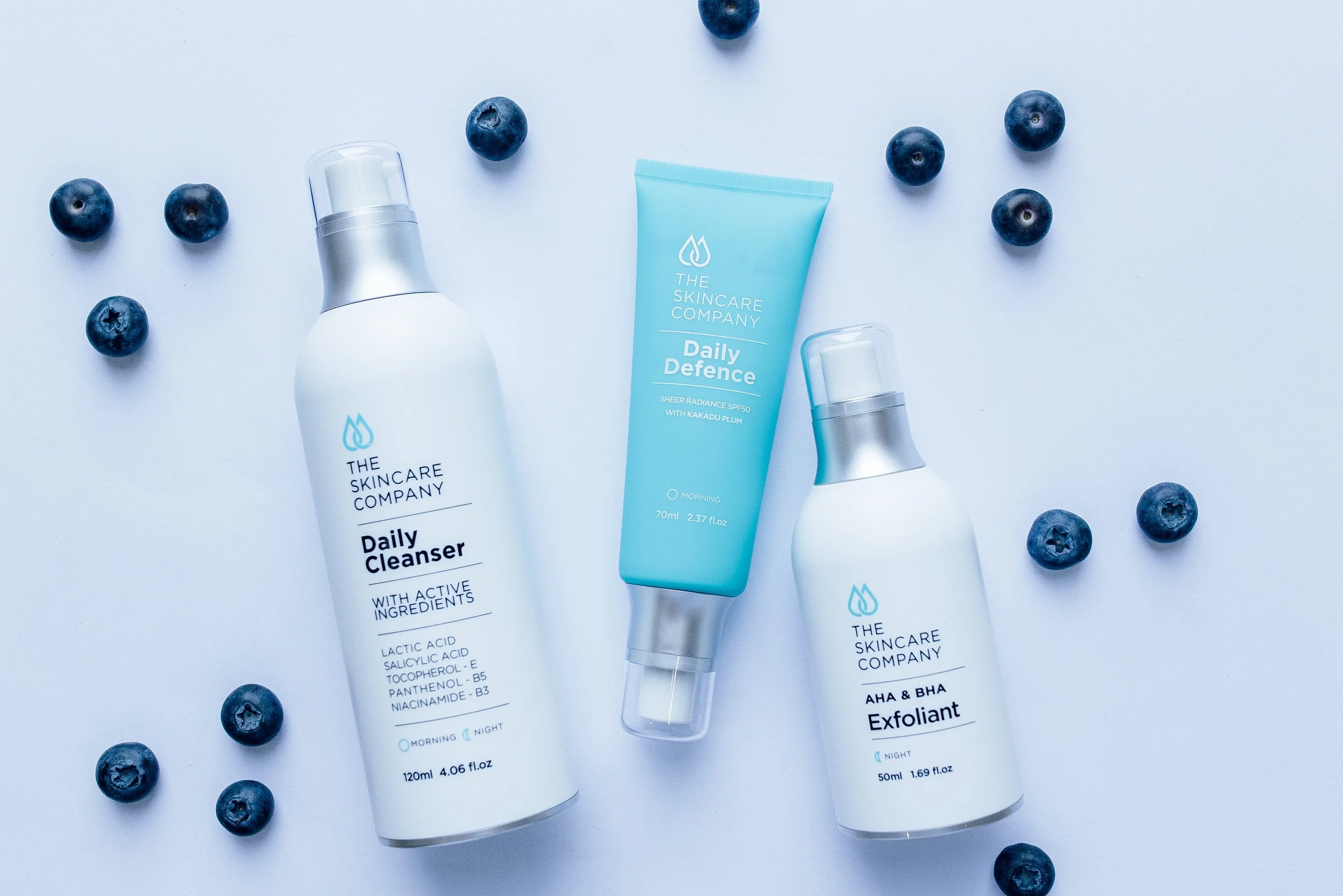 Skincare products from The Skincare Company surrounded by blueberries on a light blue background.