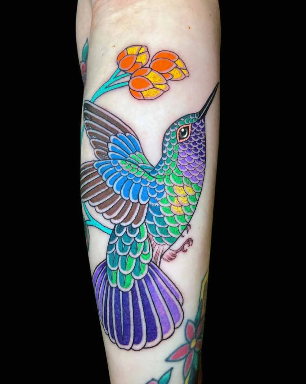Bright bold delicate neotraditional realistic style colourful tattoo of a humming bird on a womans forearm 