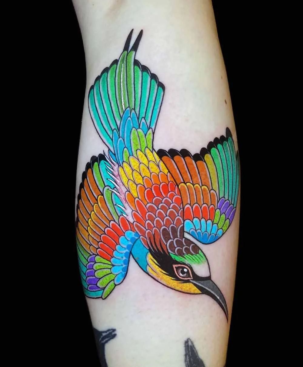 Bright bold delicate neotraditional realistic colourful tattoo of a european bee eater bird on a womans forearm 