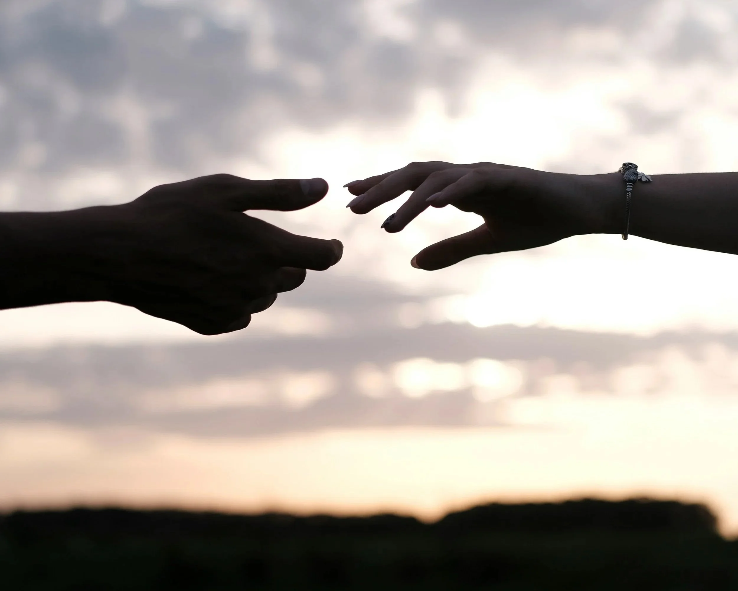 Two hands reaching out for each other against a sunset