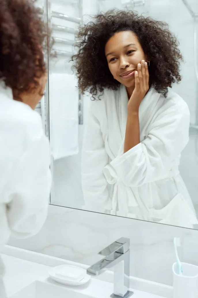Smiling woman touching her face while looking in a bathroom mirror