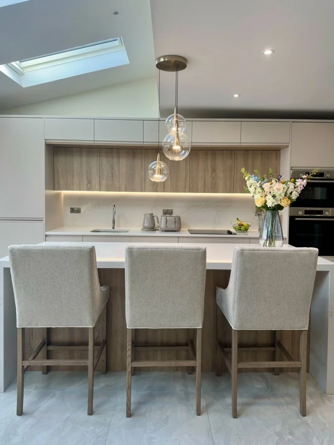 A customer’s Cashmere and oak kitchen with an island, three upholstered stools and glass pendant lights