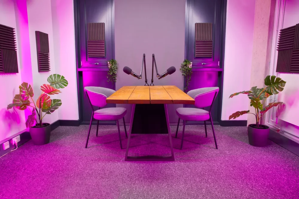 Podcast recording studio table set with two microphones, chairs and pink lighting in London