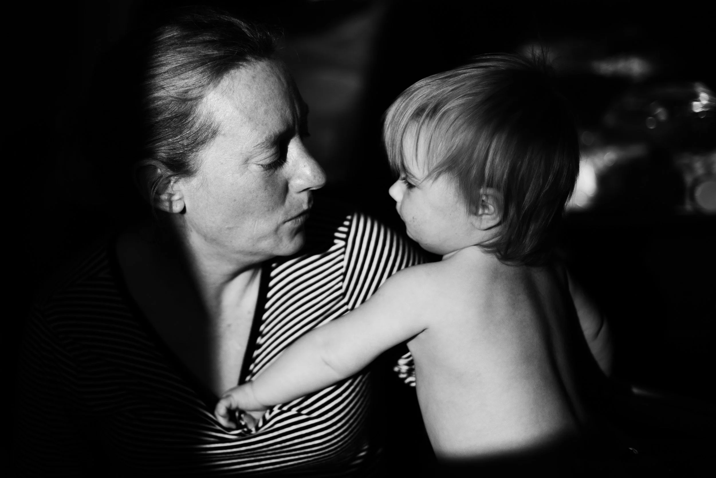 A black and white photo of a woman and a young girl looking at each other closely, with the woman gently holding the girl.