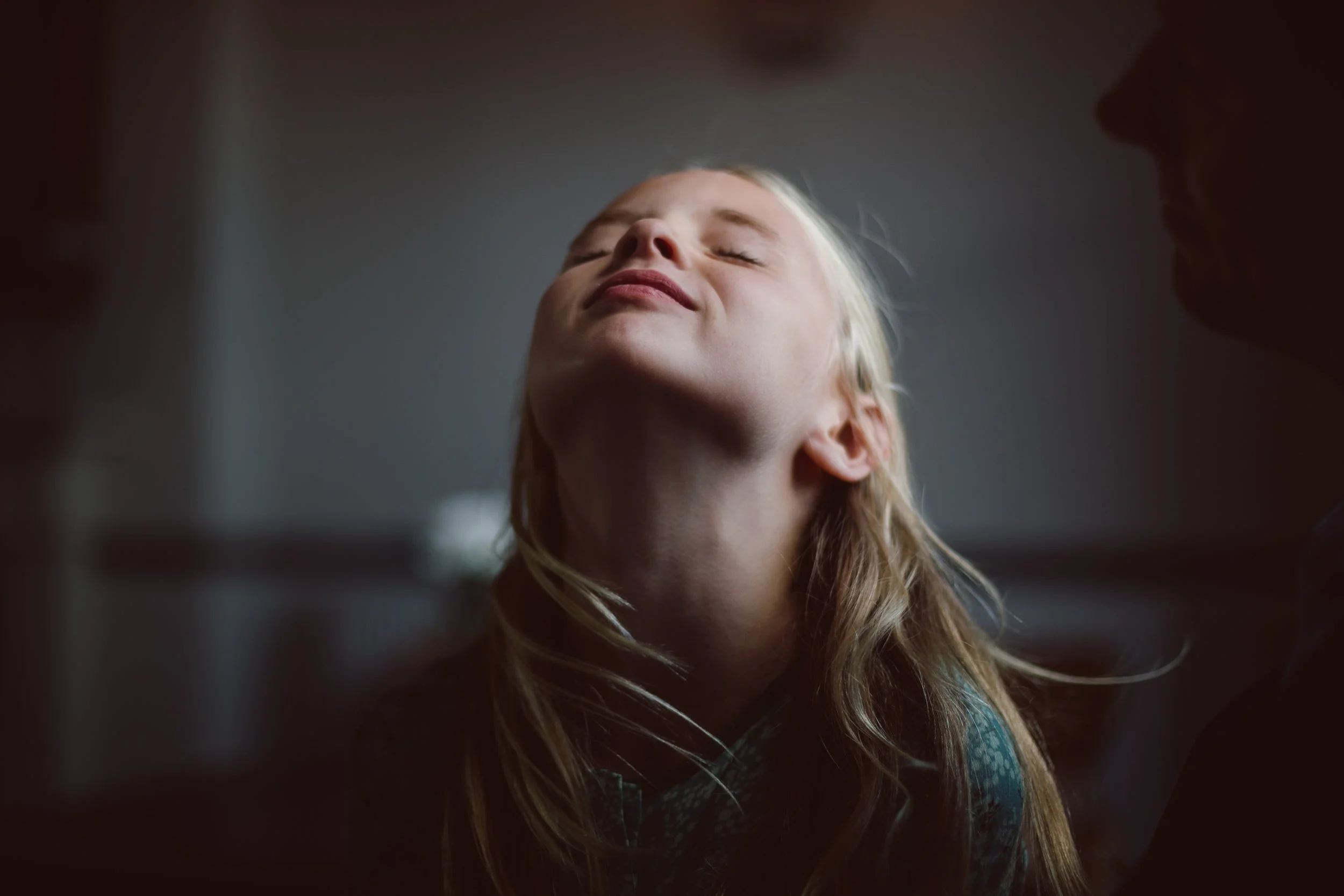 A young girl with closed eyes and a slight smile, seen from below, with some framing darkened edges around the image.