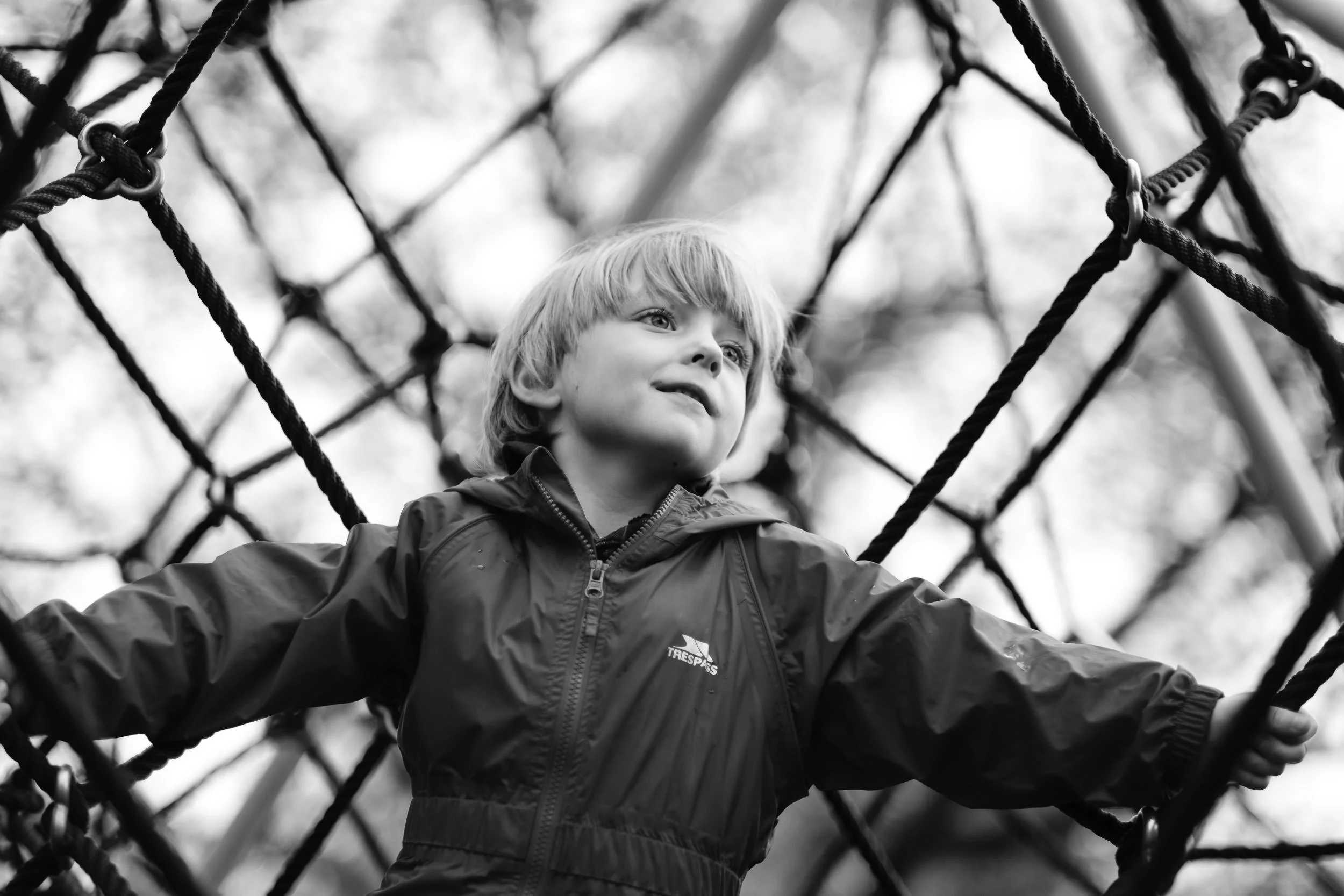 Young boy climbing on a rope net at a playground outdoors.