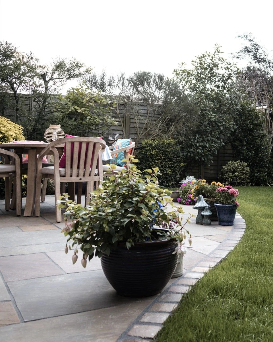 Beautifully landscaped garden with curved lawn borders, colourful planting and outdoor dining area.