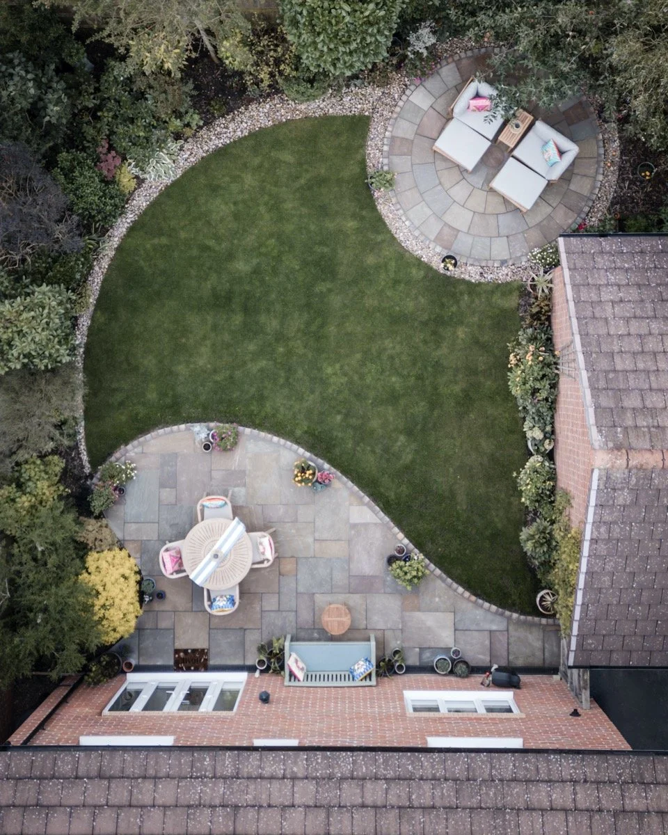 Aerial view of a landscaped rear garden featuring two patio seating areas and a central lawn.