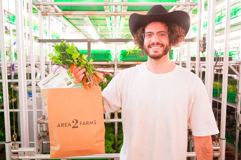An Area 2 Farms farmer in a cowboy hat holds a bag of the week's harvest