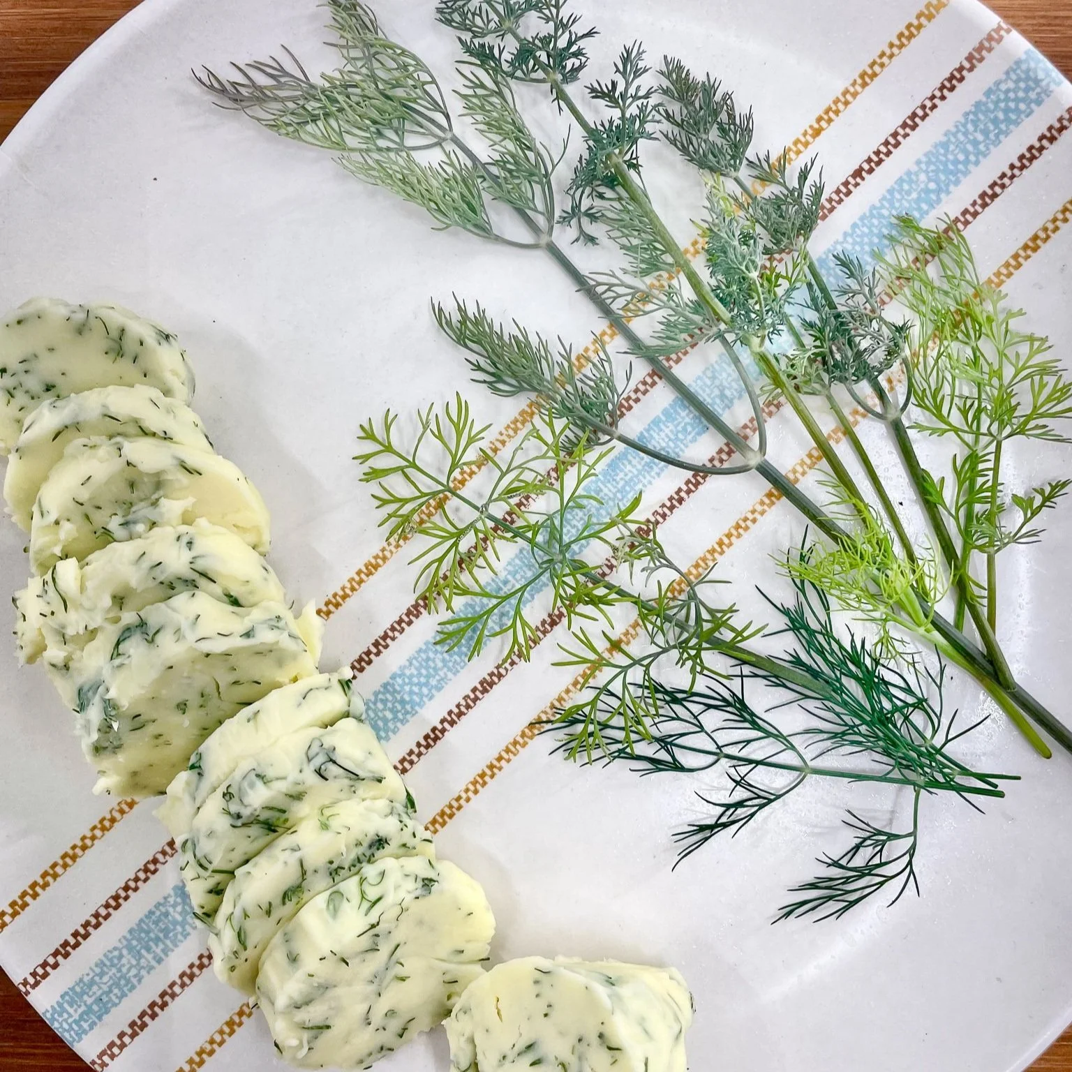 Large sprigs of dill on plate with sliced log of herb butter