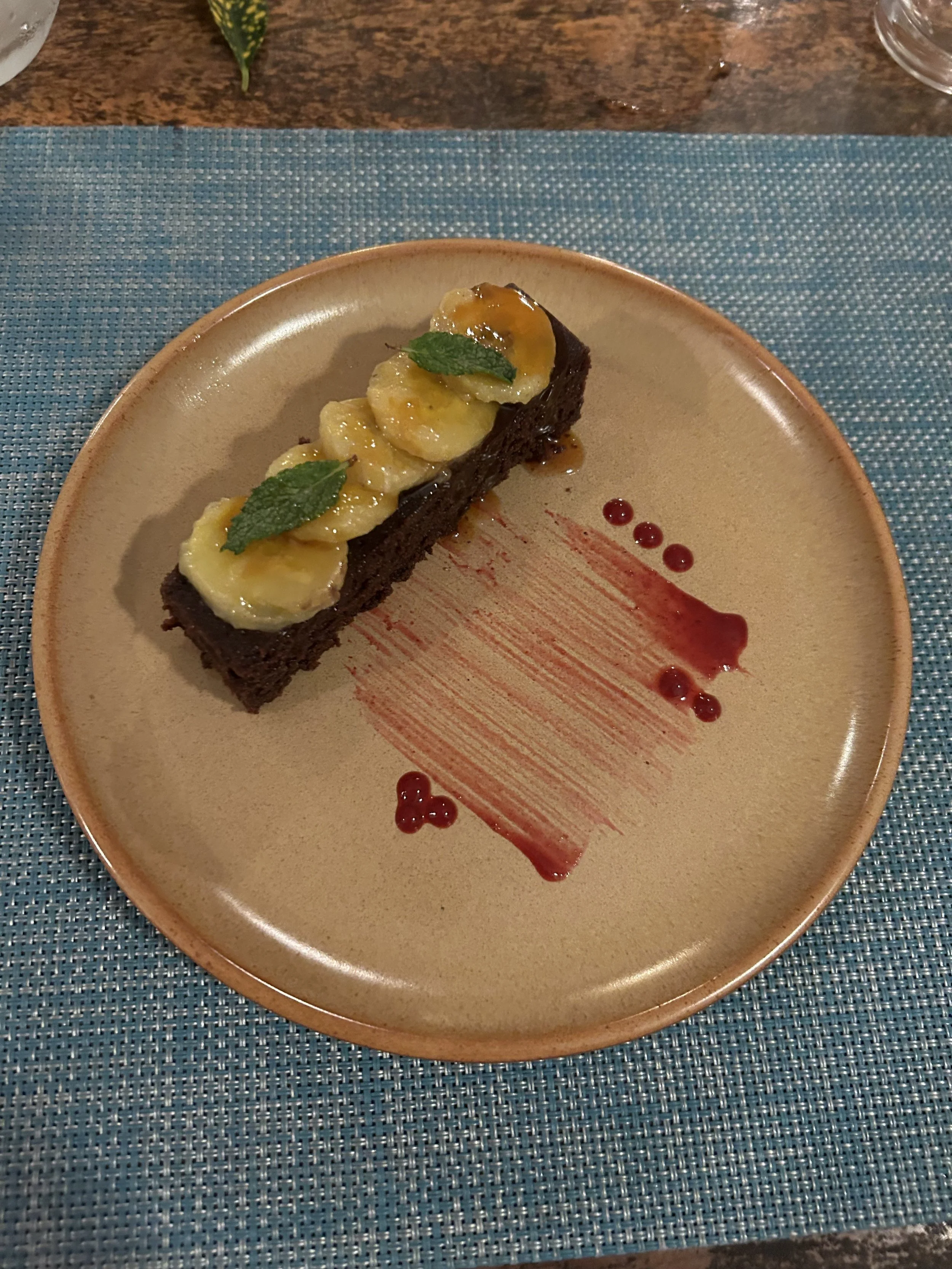Chocolate cake topped with banana slices and mint leaves on a plate with red sauce drizzle.