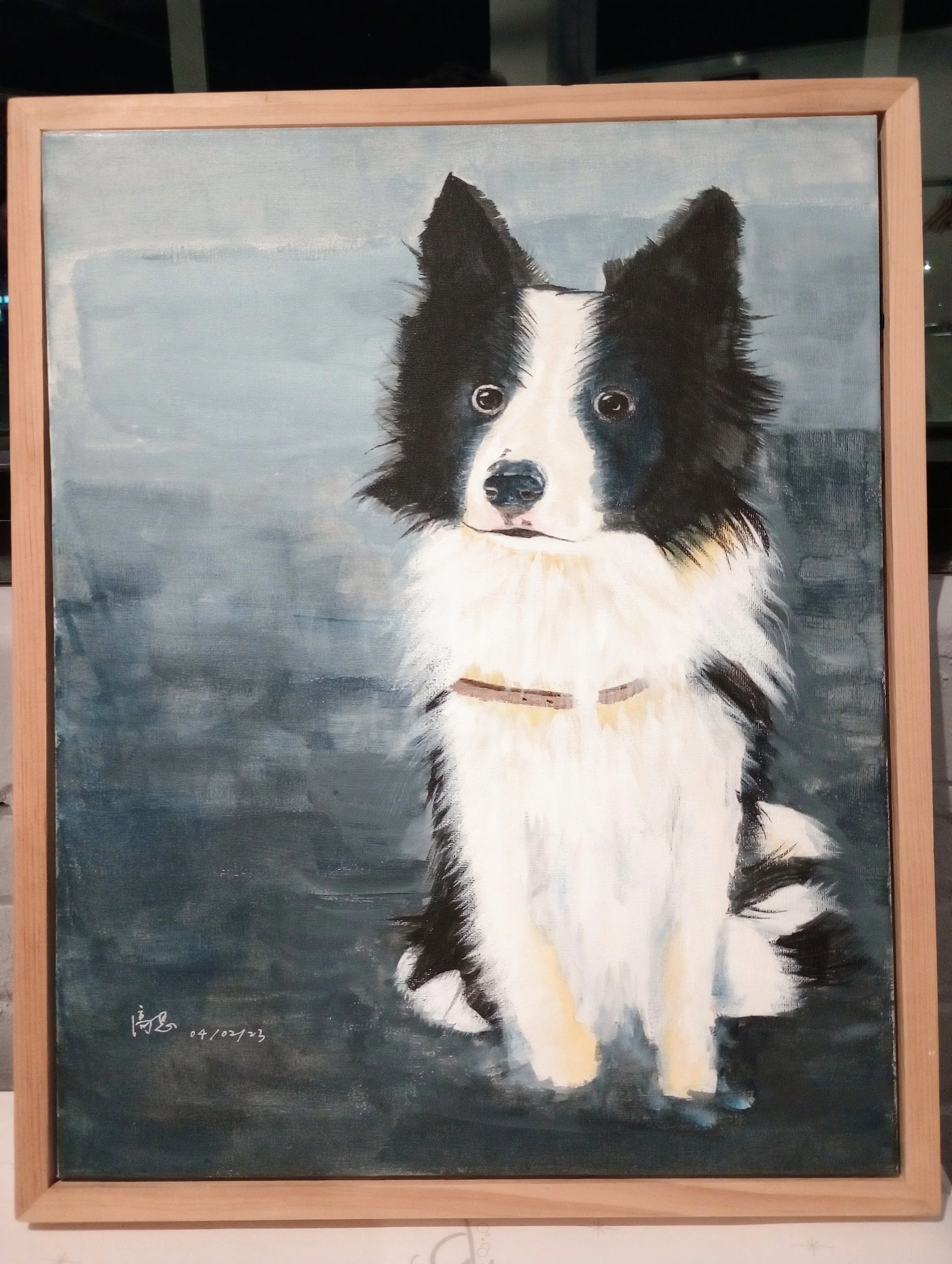 Painting of a black and white dog with fluffy fur on a blue background, framed in a wooden frame.