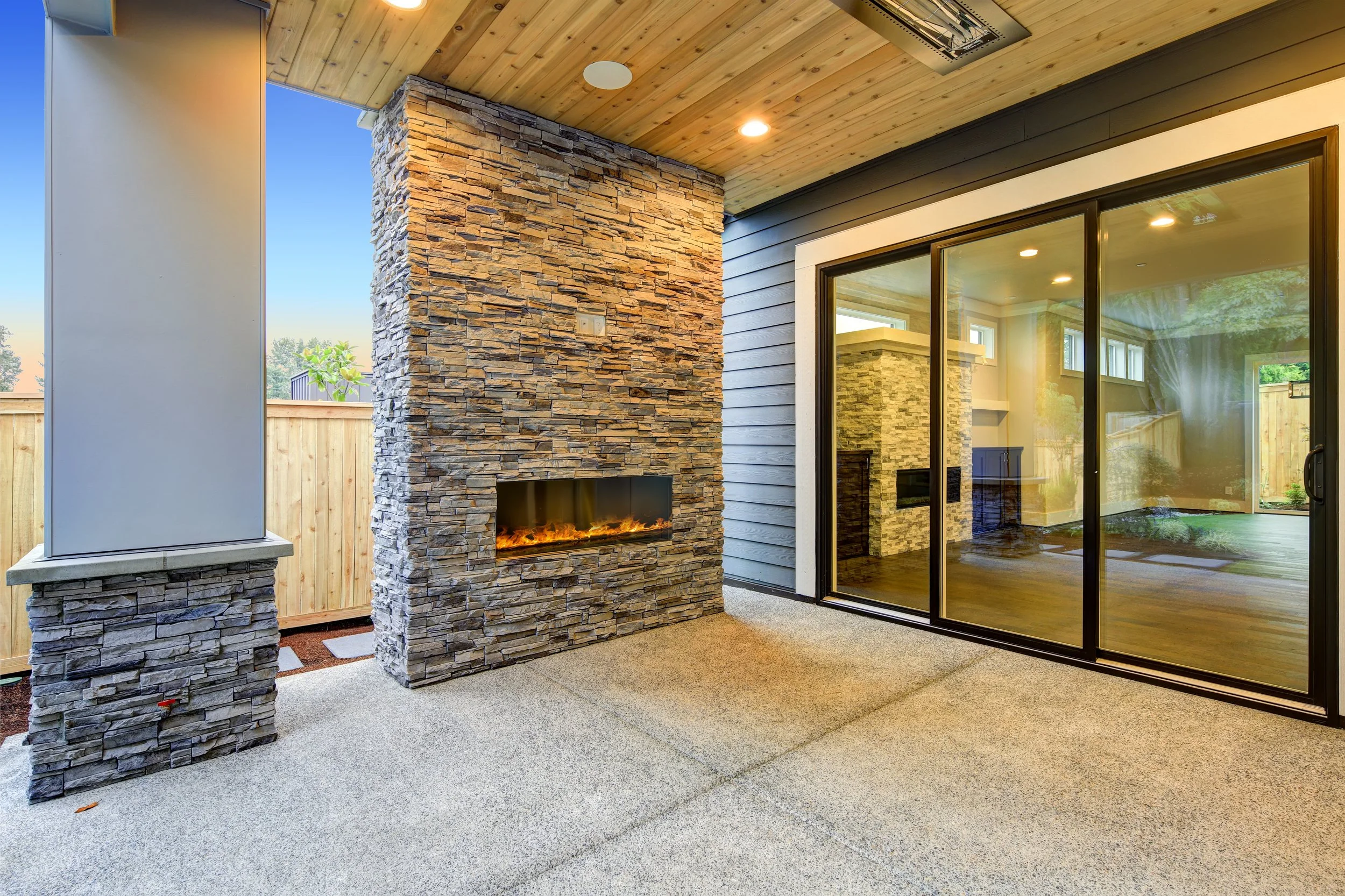 Outdoor covered patio with a stone fireplace and large sliding glass doors leading to an indoor living space.