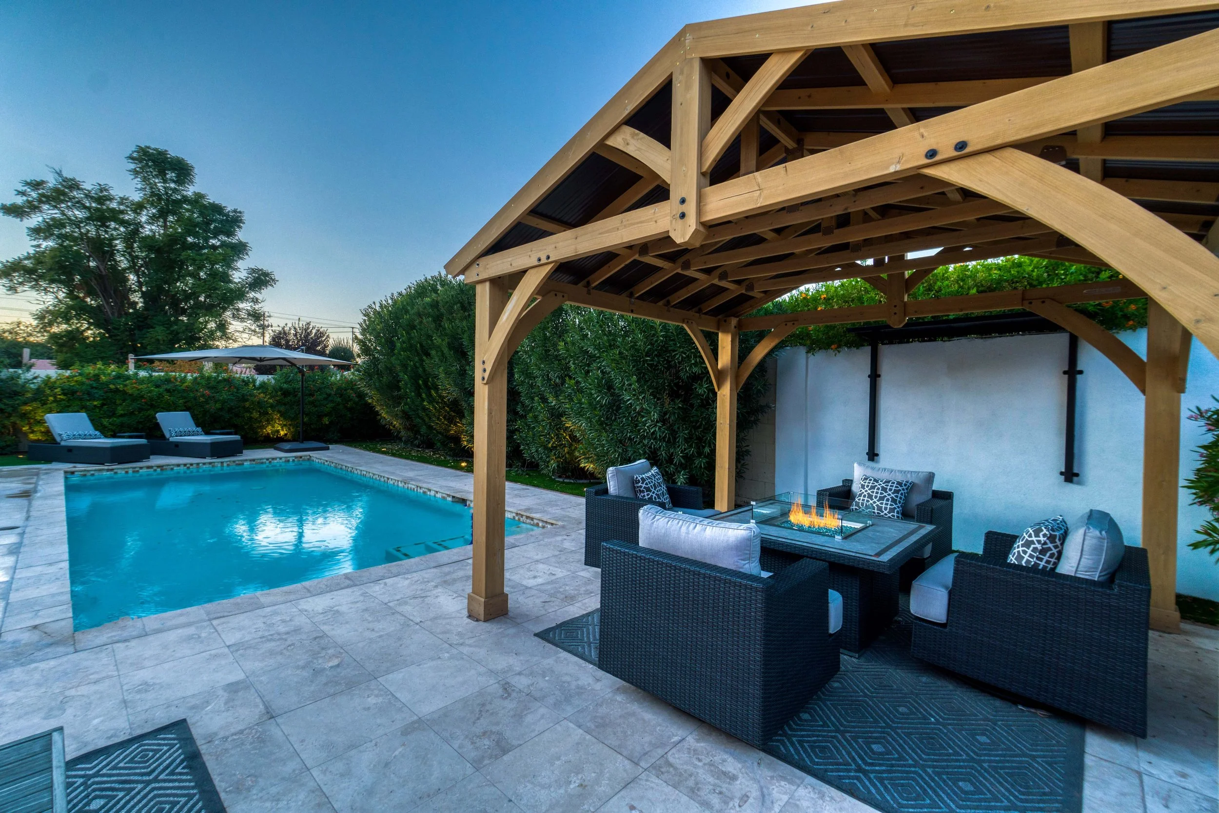**Alt Text:** Private pool area with Belgard pavers, gas fire table, and privacy landscaping creating a comfortable outdoor living space in Bear, Delaware