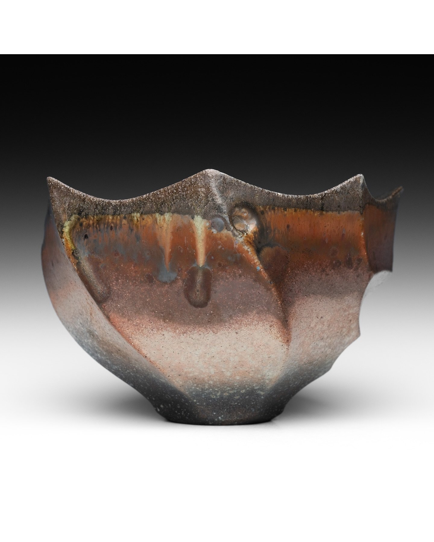 A faceted teabowl with dramatic wood ash drips, gradients of burgundy flashing, and shimmery reflective surfaces. The distinct horizontal bands of surface variation on this piece are the result of how it was loaded&mdash;it was nestled inside of a la