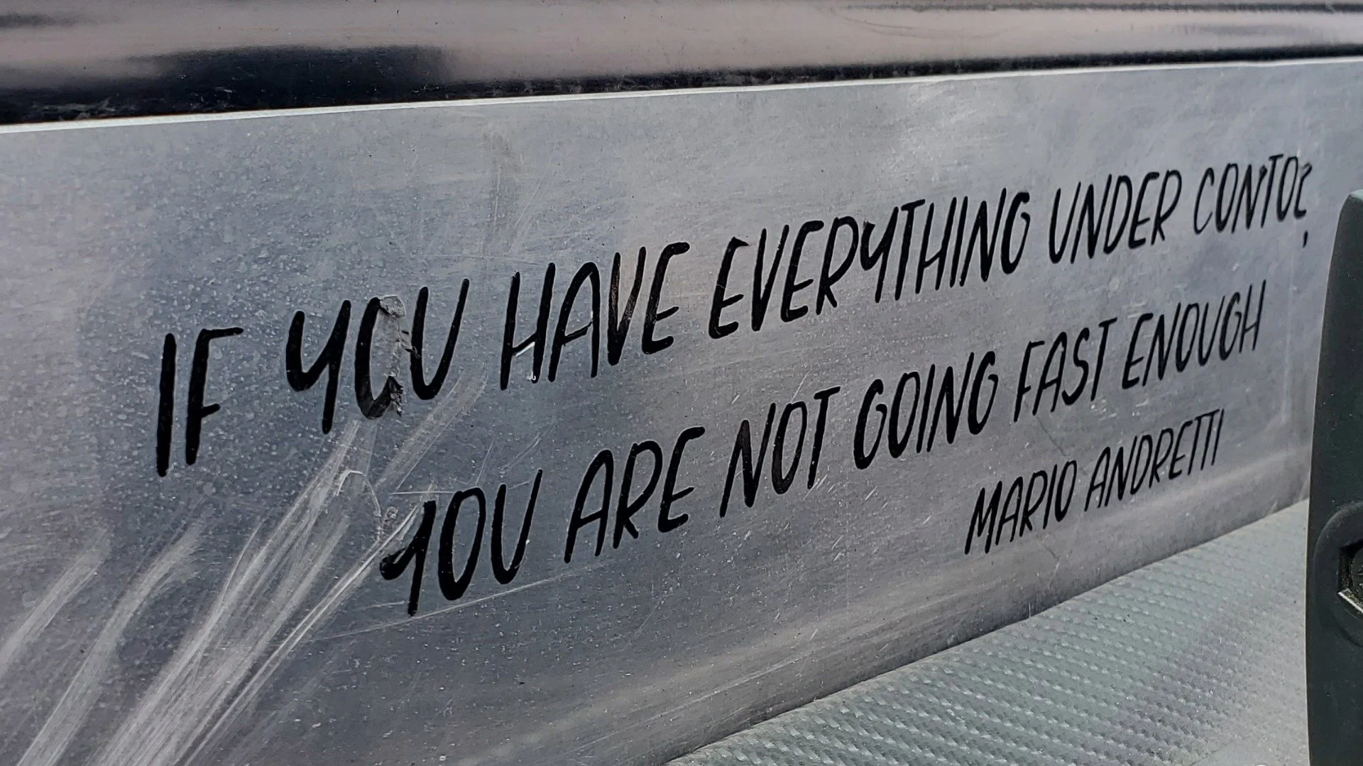 A quote etched into a car dashboard by Mario Andretti that reads "if you have everything under control you aren't going fast enough"