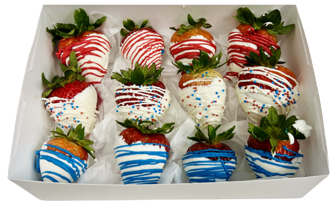 A white box filled with strawberries dipped in white chocolate and decorated with red and blue drizzle and sprinkles, perfect for the 4th of July.