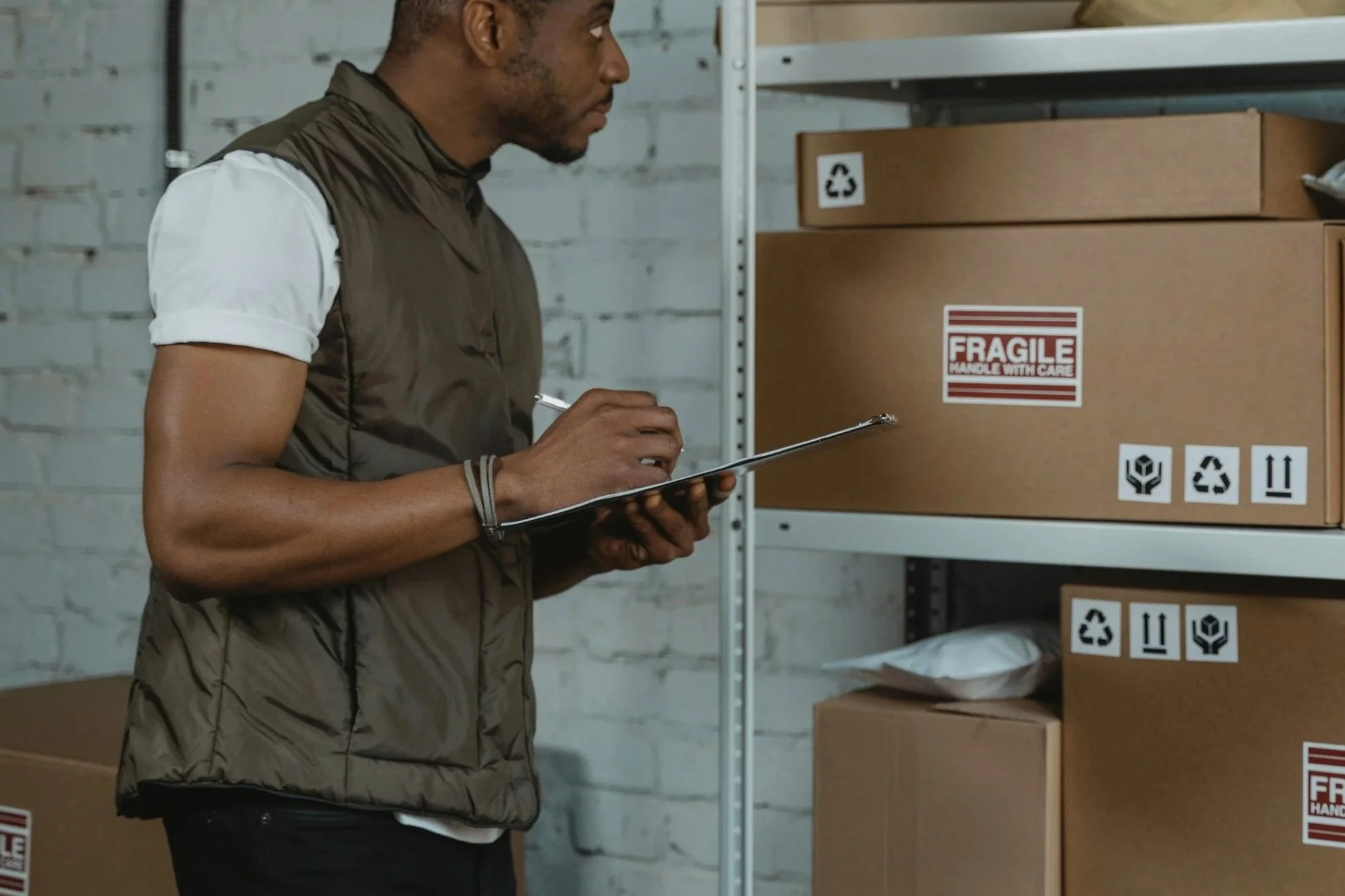 A person inspecting boxes in a warehouse, holding a clipboard and writing notes.