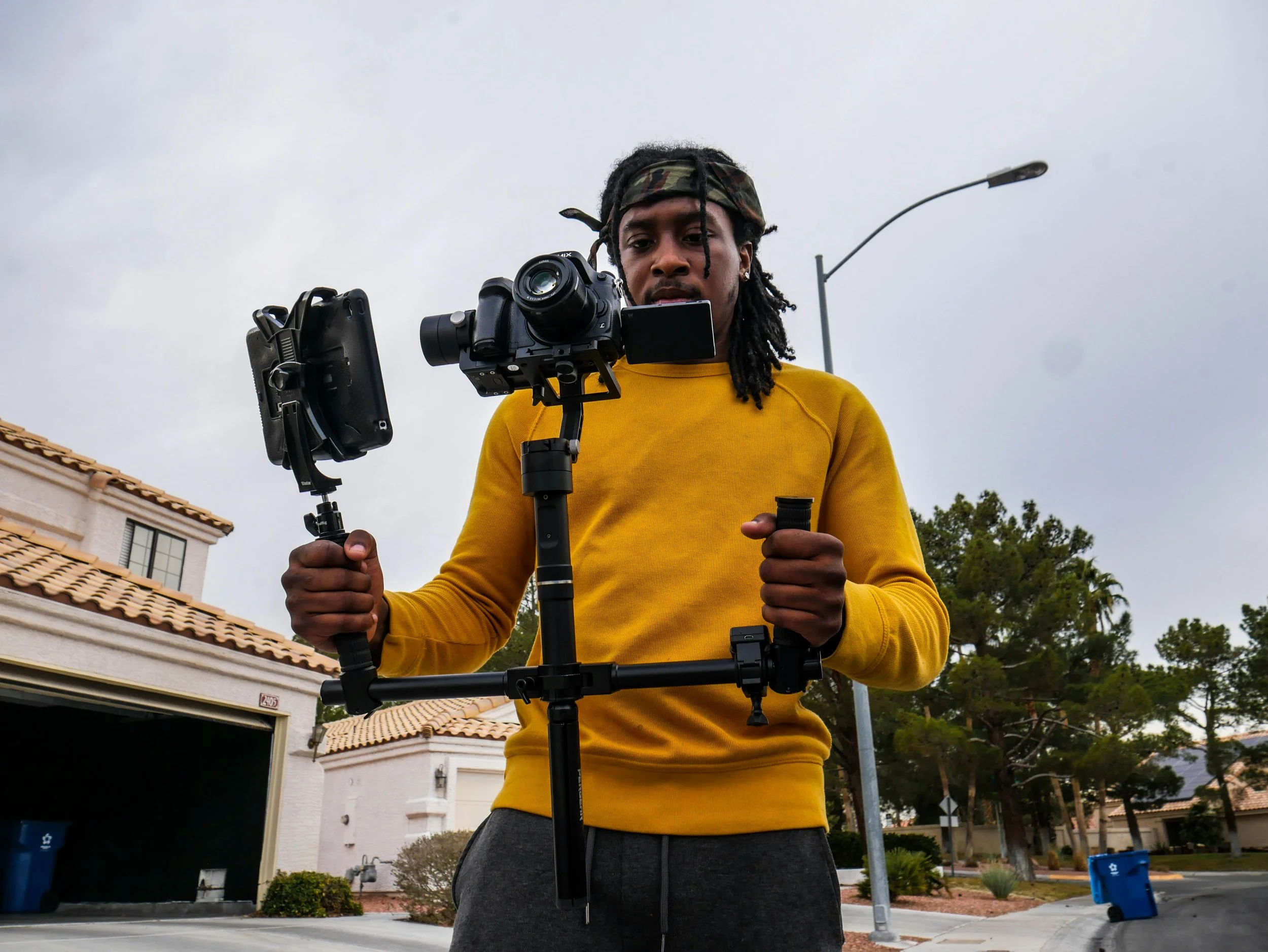 A man operating a camera rig outdoors on a cloudy day.