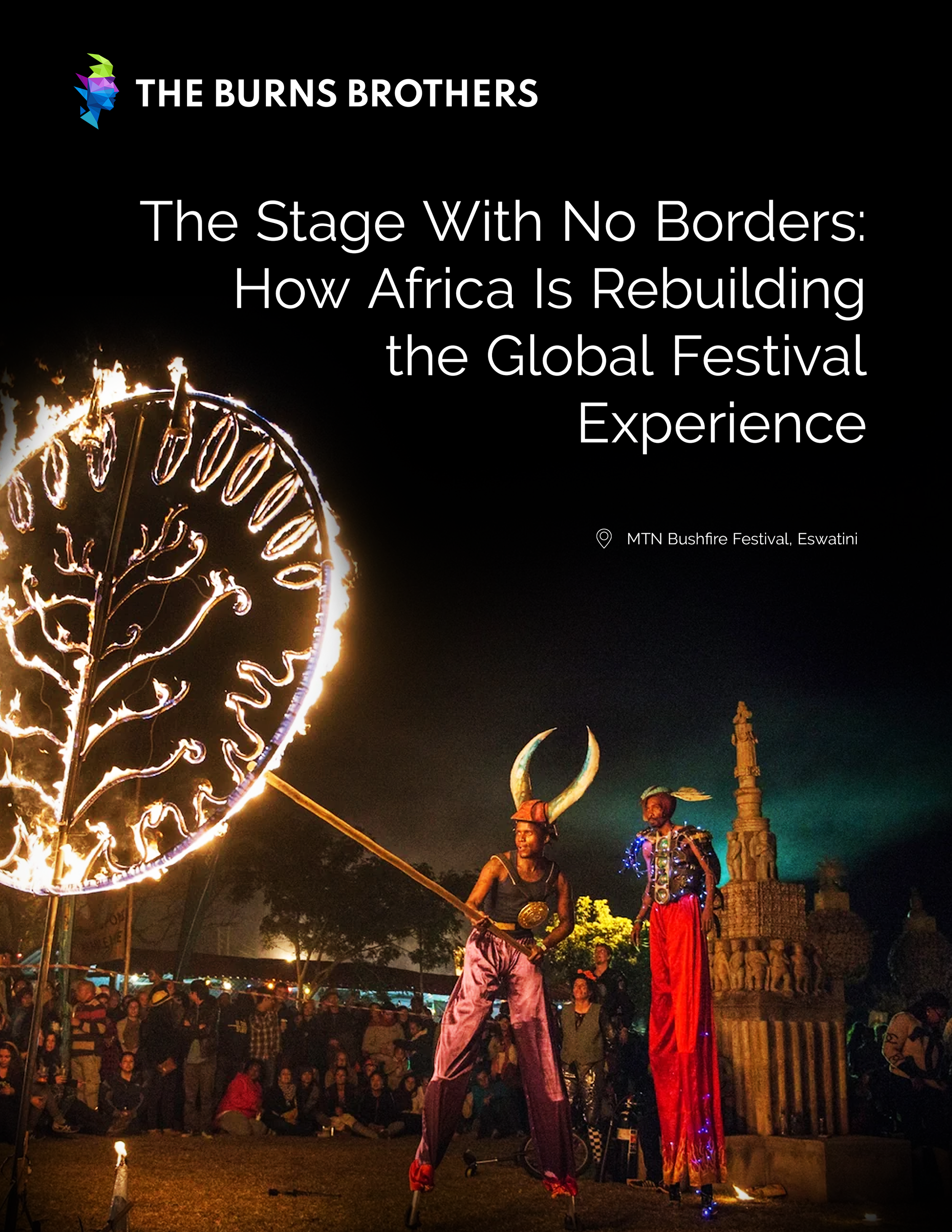 Performers on stilts in costume with a flaming fire circle at a festival in Eswatini, with a crowd watching in the background at night.