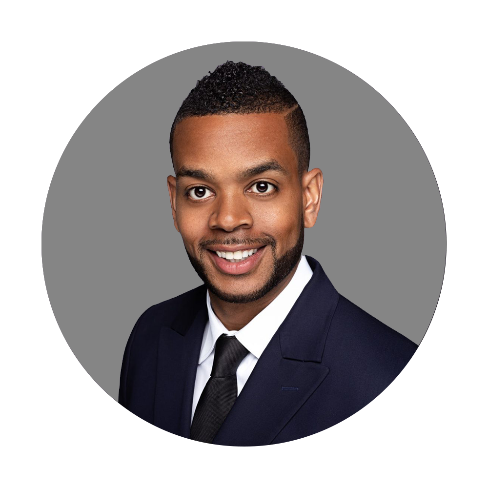 Headshot of a smiling man wearing a dark suit, white shirt, and black tie against a gray background.