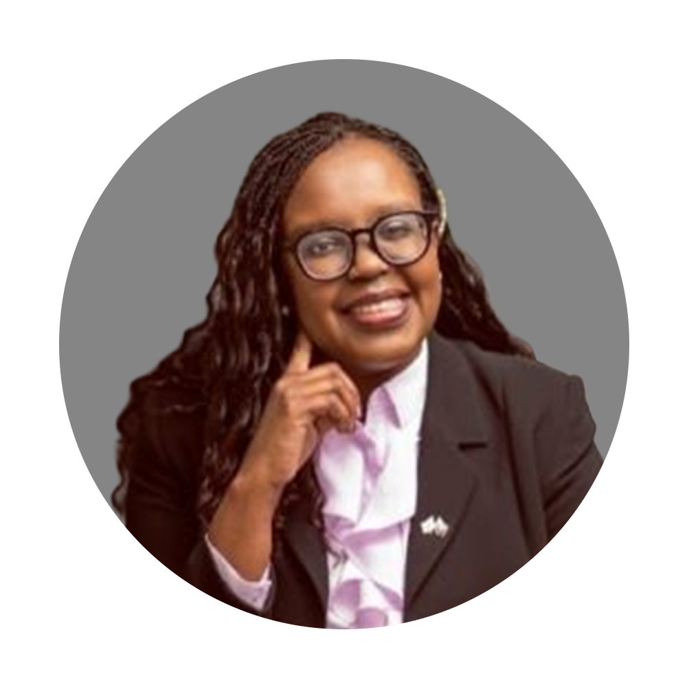 A woman with glasses and braids wearing a black blazer and white shirt, smiling and resting her chin on her hand