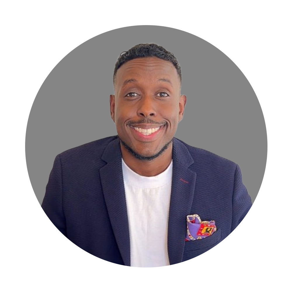 A smiling man in a navy blazer with a white shirt, featuring a colorful pocket square, against a gray background.