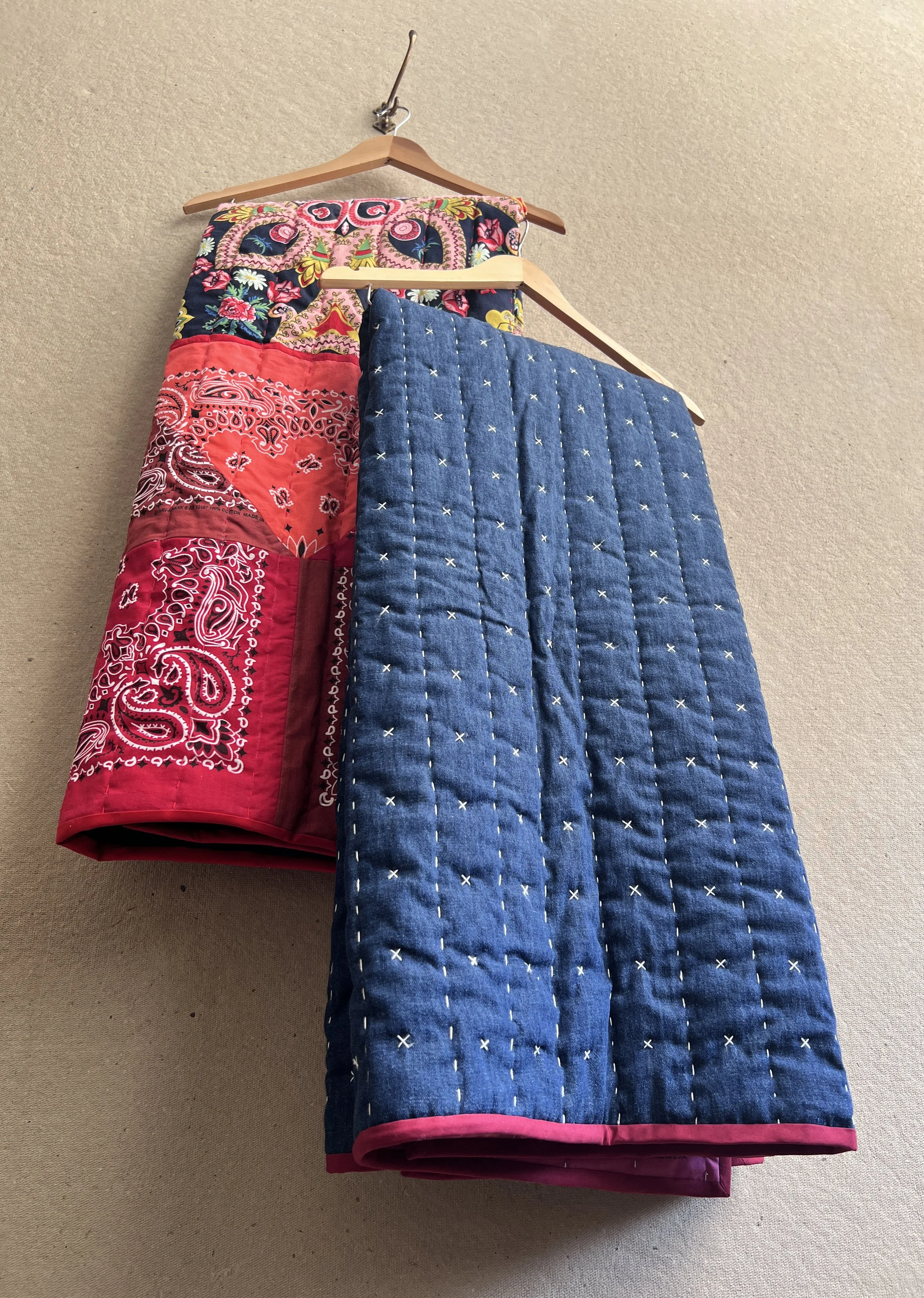 Two hanging blankets of the same style showing the inside with bandanas, and outside with running stitch and X embroidery