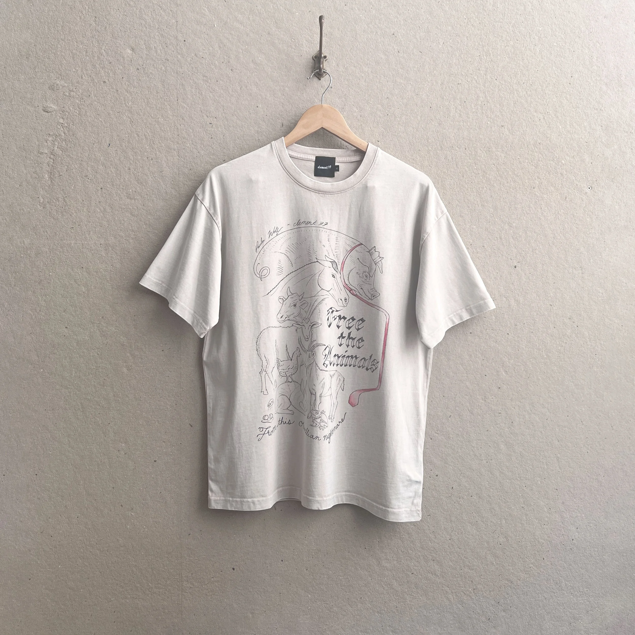 T-shirt hanging on a hook with a light wood hanger. T-shirt is oversized with "free the animals" graphic.