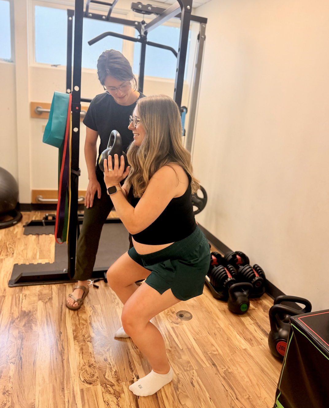 A pelvic floor therapist guides a pregnant client through exercise in a gym.