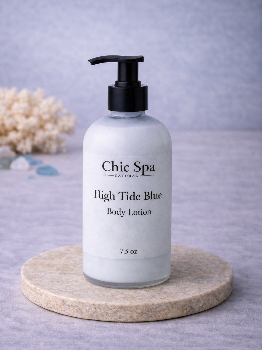Chic Spa Naturals High Tide Blue Body Lotion in a frosted glass bottle with black pump on a stone display with coastal-inspired background accents.