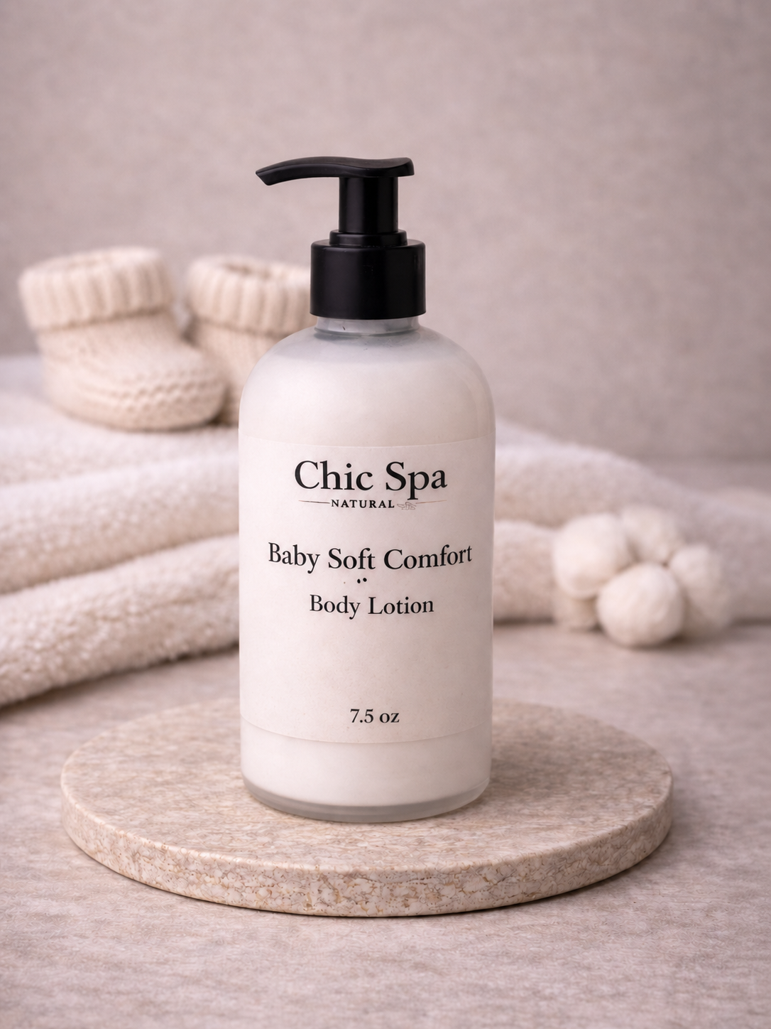 Chic Spa Naturals Baby Soft Comfort Body Lotion in a frosted glass bottle with black pump on a stone display with soft neutral background.