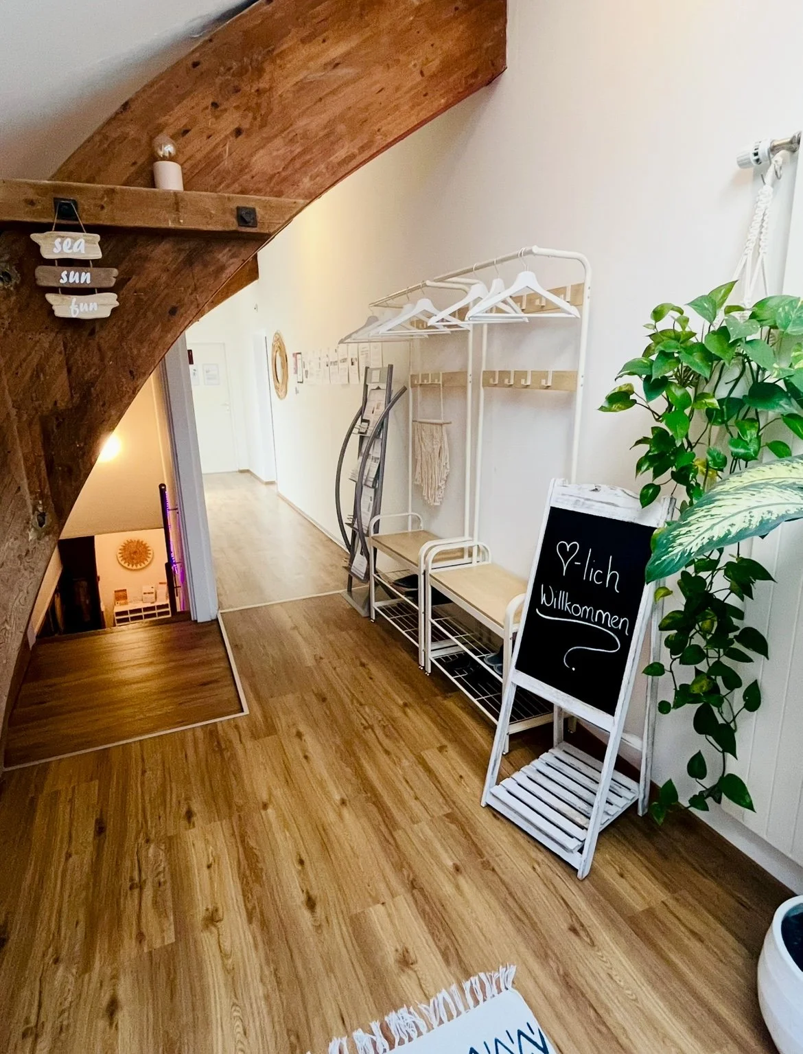 Eingangsbereich mit Willkommensschild, Pflanzen, Garderobe, Hockergestell und Treppe, Holzdeckenbalken, Holzfußboden.