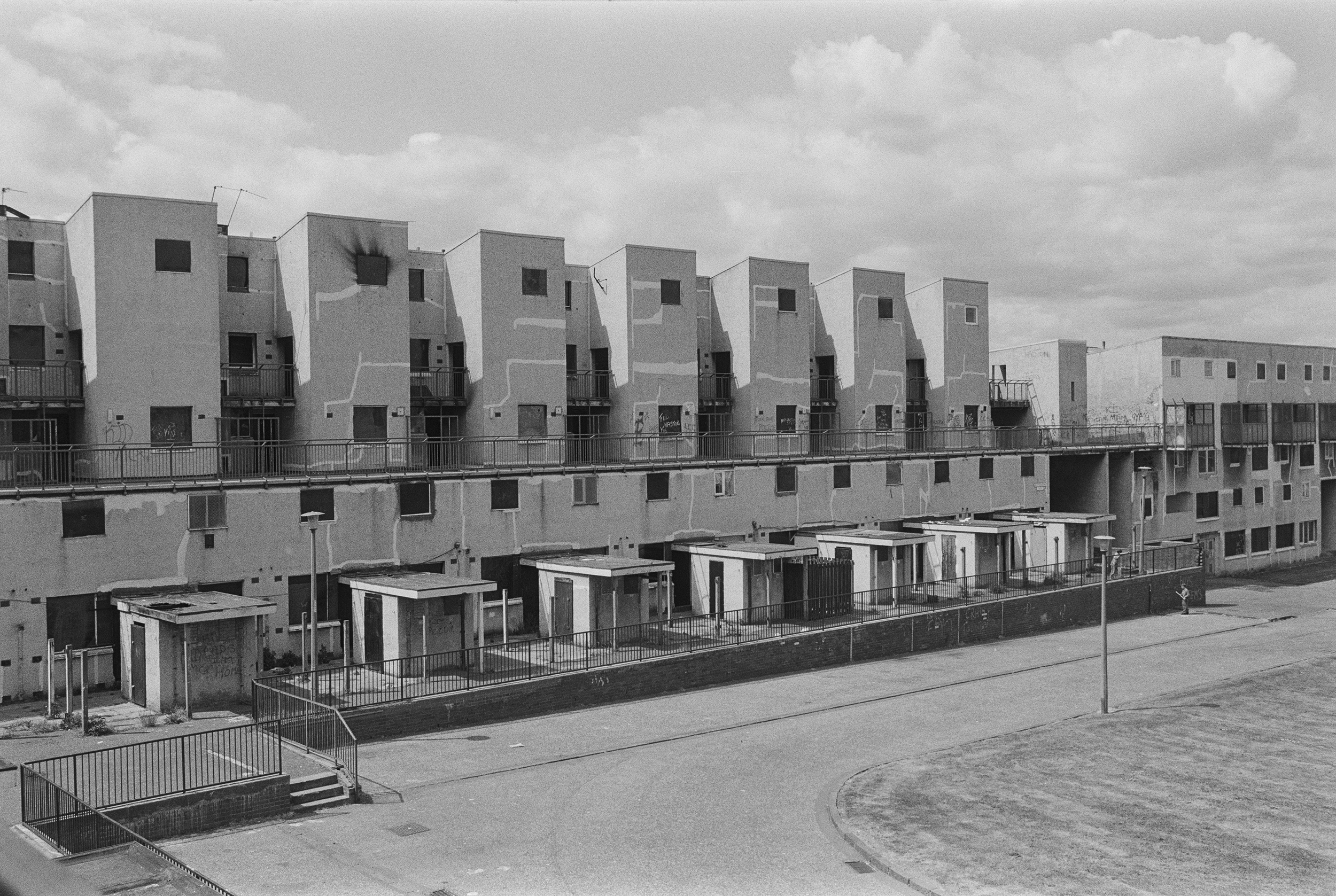 Image description: black and white landscape image of seven blocks of flats in Granton. The blocks are in brutalist style, with a square entranceway in front of each, and are identical. The top window of the block that is second from the left is fire