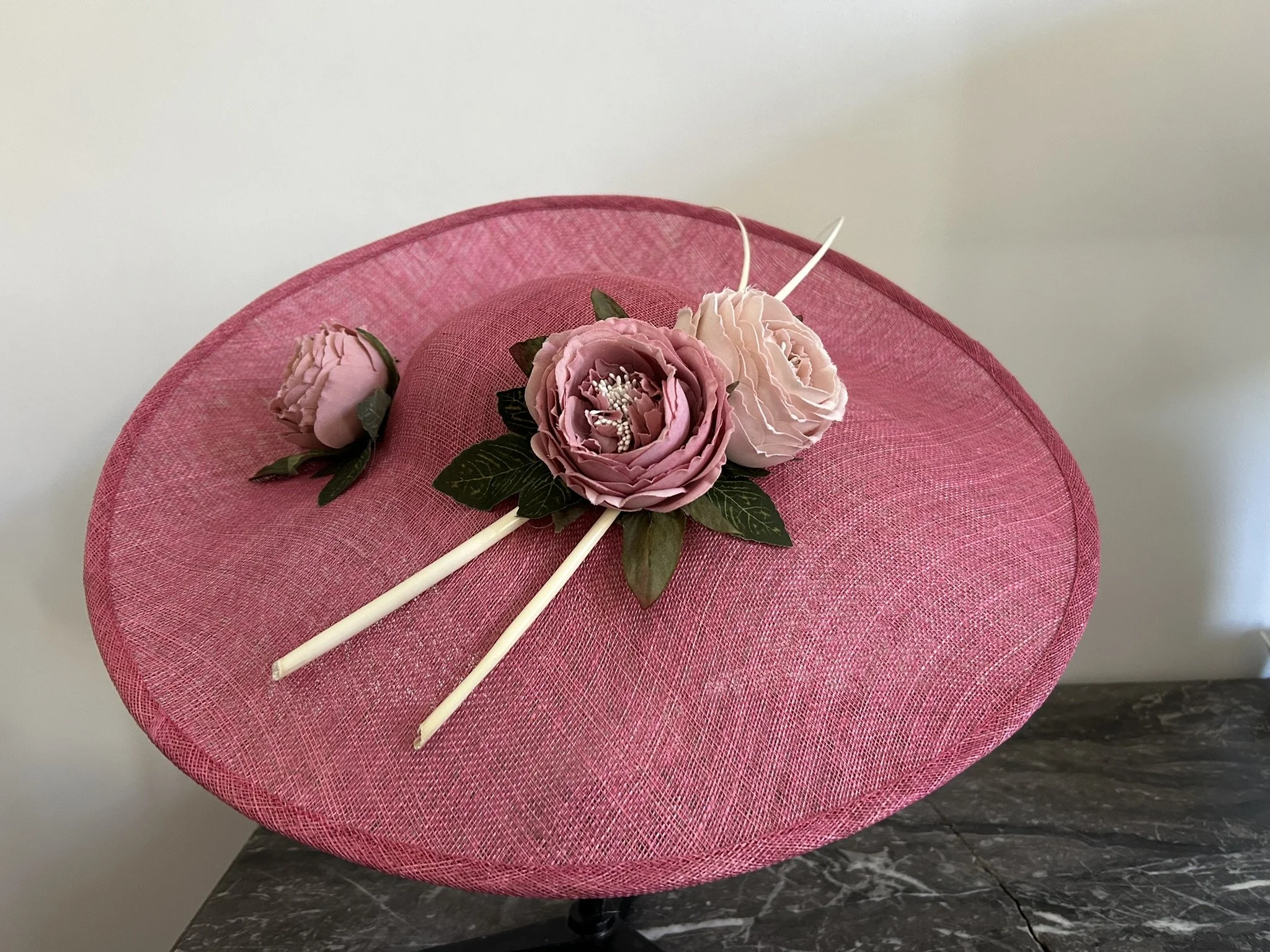 Chapeau de grande taille en sisal beige et rouge, placé sur un mannequin, avec une fleur blanche en décoration à côté.