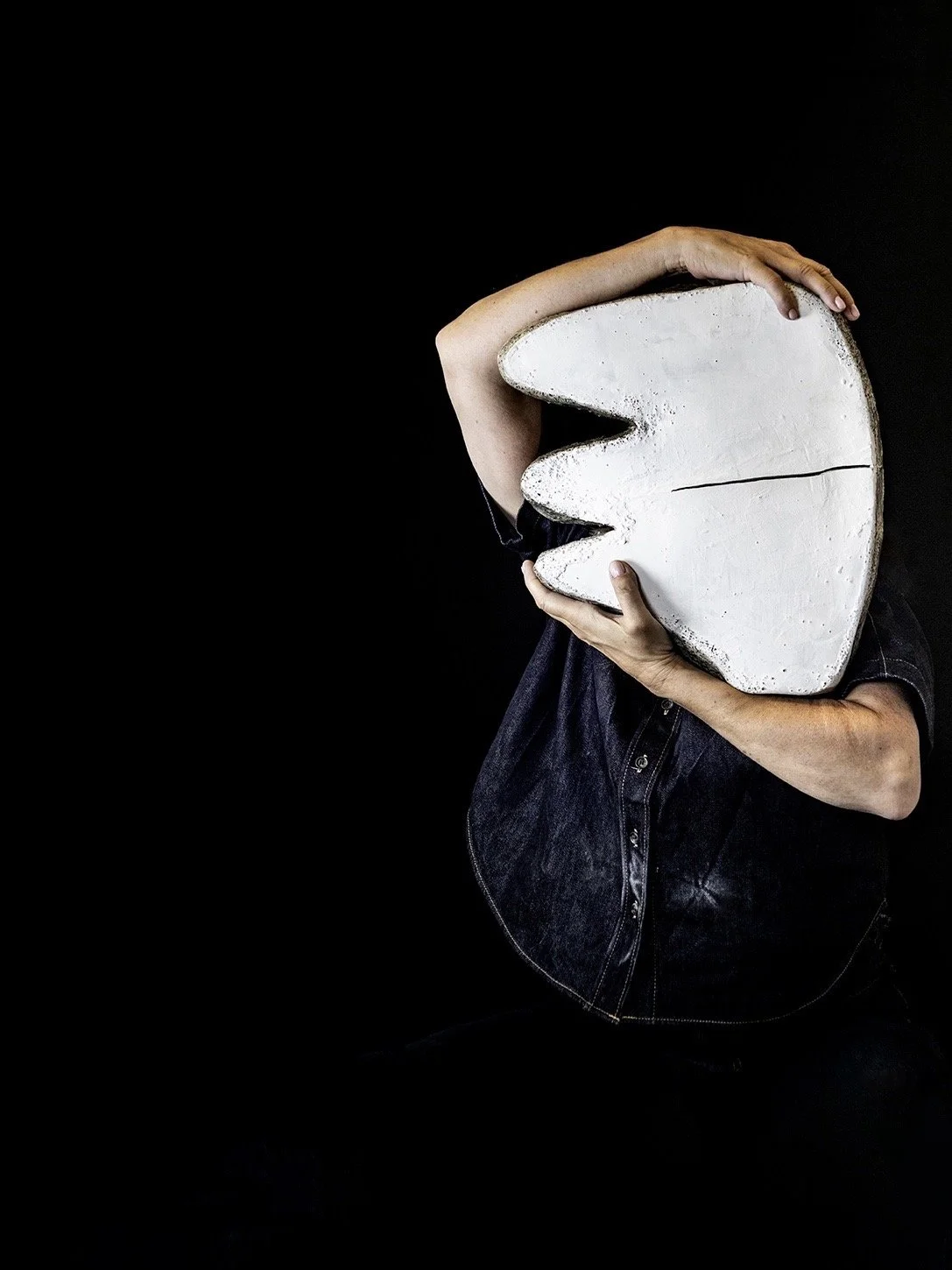 Person holding a large, speech bubble-shaped object in front of their face, obscuring their identity, against a black background