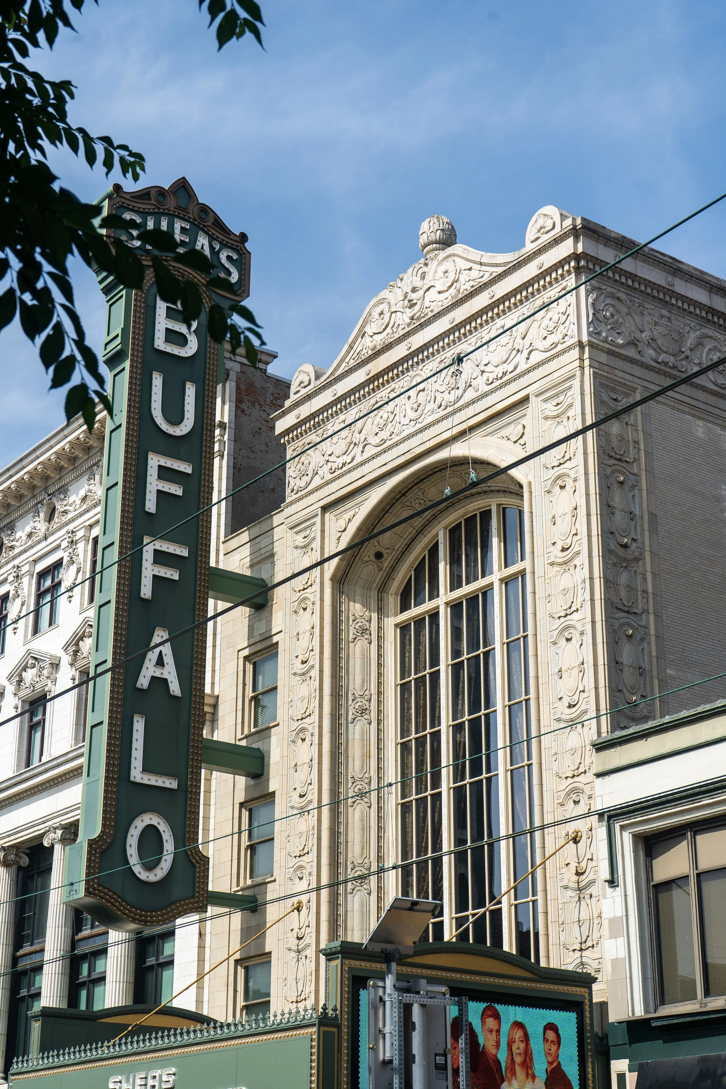 A vintage theater building with ornate architecture and large arched windows. A vertical sign reads 'SHEA'S.'