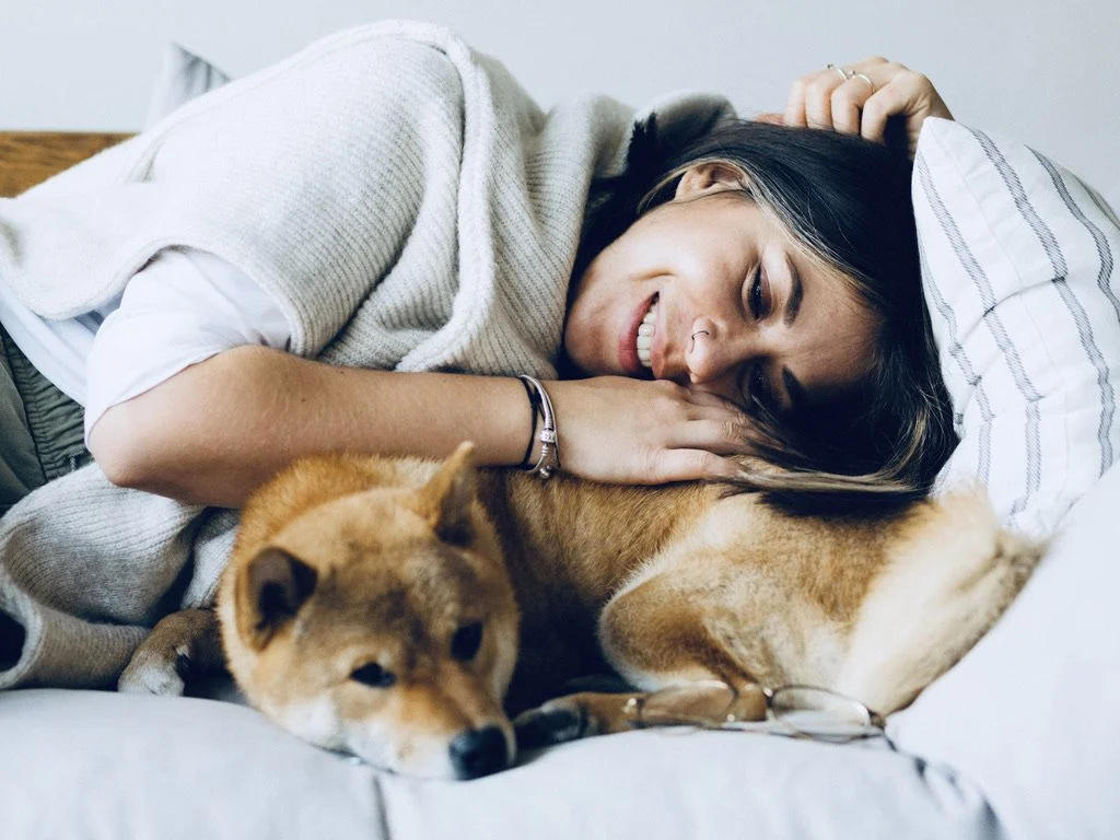 A woman lying on a bed, smiling, with a Shiba Inu dog lying beside her, cuddling close. Fairfield ct green cleaning services near me, green house cleaning services near me, green home cleaning services, green clean house cleaning fairfield ct