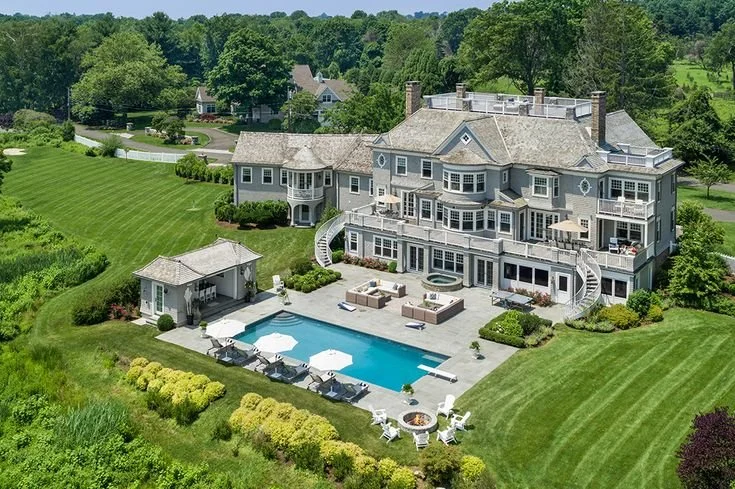 Large luxury house with a backyard pool, surrounded by lush green grass and trees.