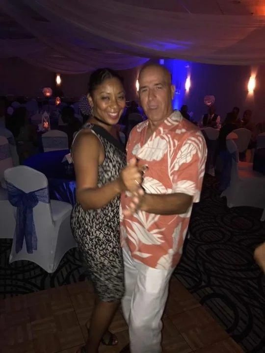 A man and woman dancing together at a celebration or party in a decorated venue with tables and chairs.
