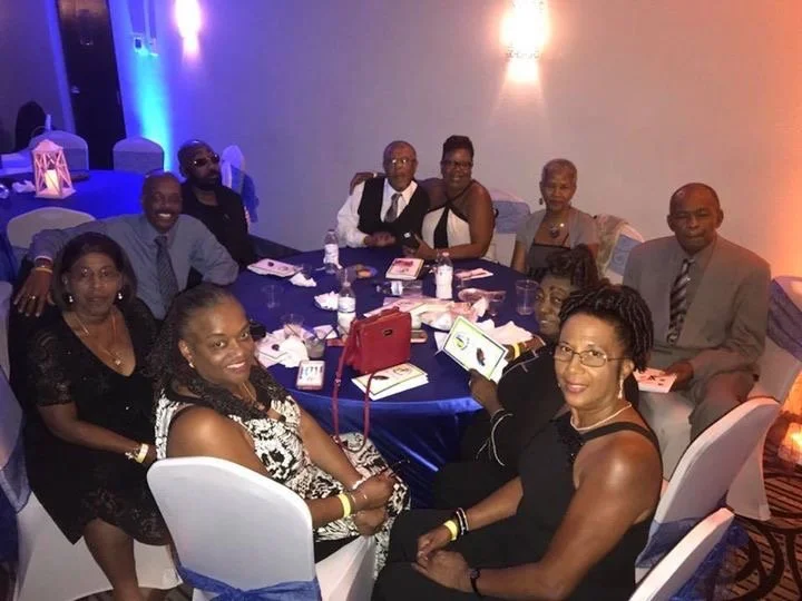 Group of well-dressed people sitting around a decorated banquet table at a formal event or celebration.